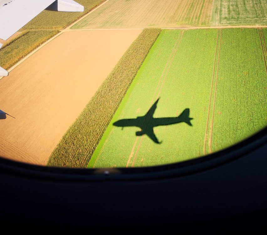 Aeriel view of an airplane shadow looking out of an airplane window over a field